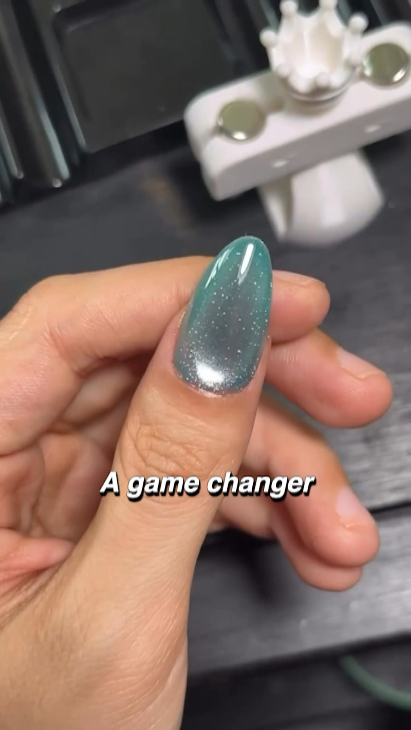 A close-up shot of an automatic magnetic wand hovering steadily over a shimmery cat eye gel nail, instantly pulling particles into a clean velvet line.