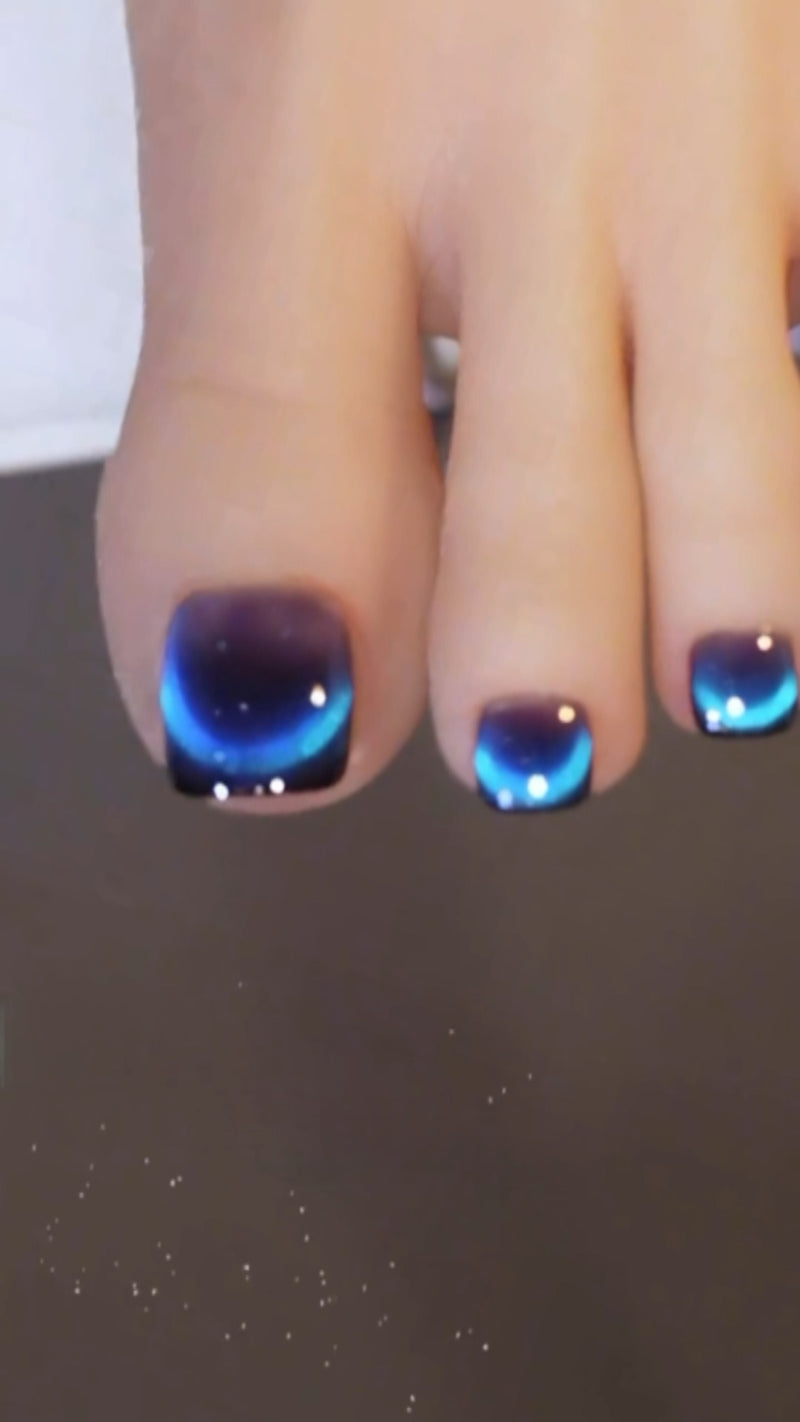 A beautiful aesthetic close-up of long stiletto nails featuring a dark black ombré base and a shimmering, magnetic blue cat eye French tip.