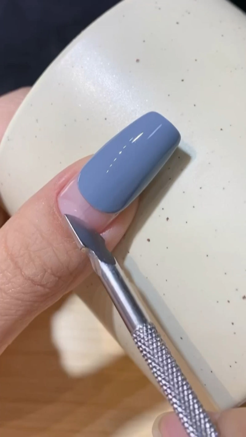 A close-up view of a brush painting thick gel remover onto a fingernail, showing the old polish starting to bubble up and break apart.