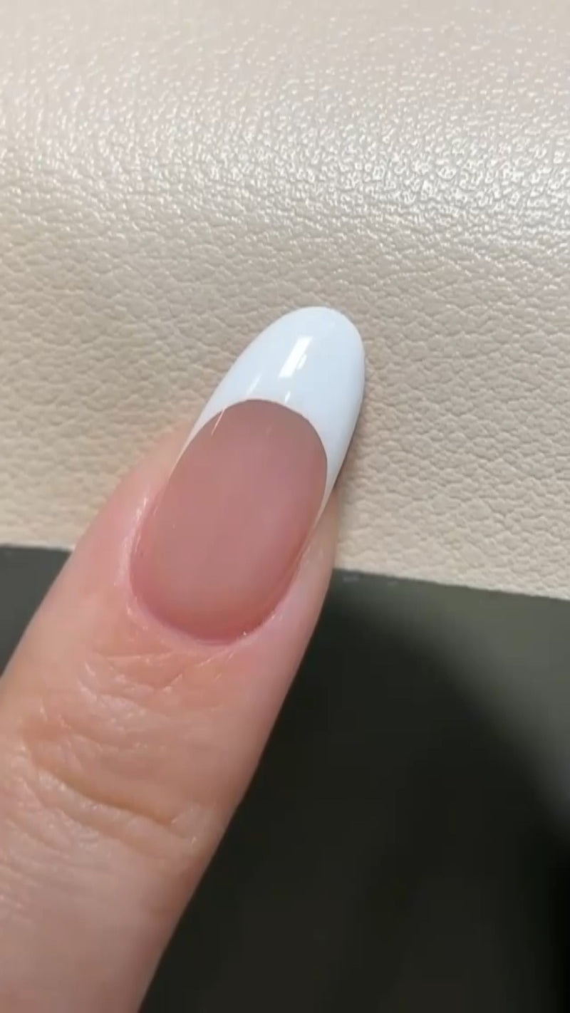 Close-up of a fine nail art brush drawing a white French tip smile line on a manicured nail.