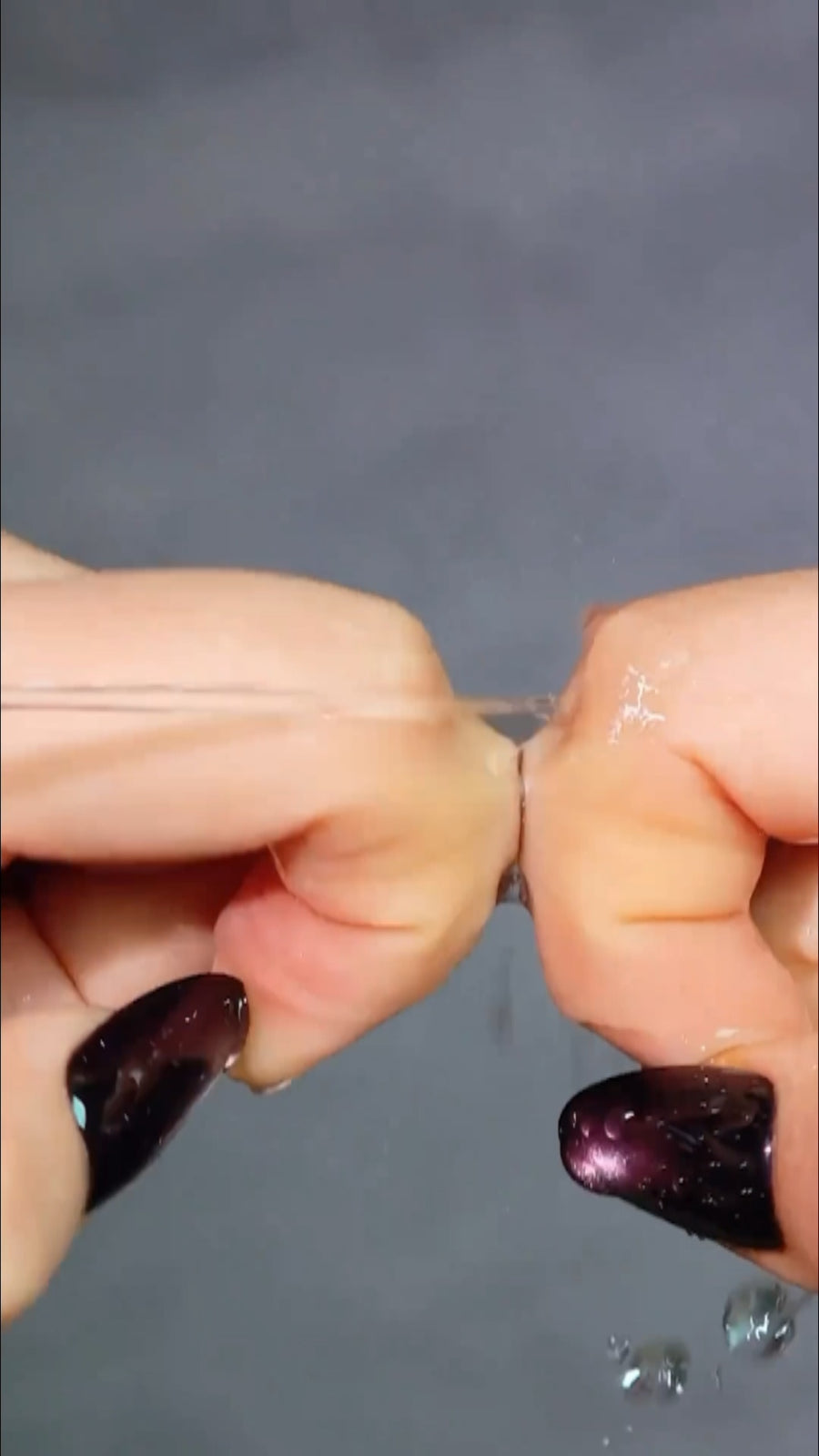 Tweezers peeling the clear protective plastic film off a double-sided nail adhesive tab applied to a natural nail.
