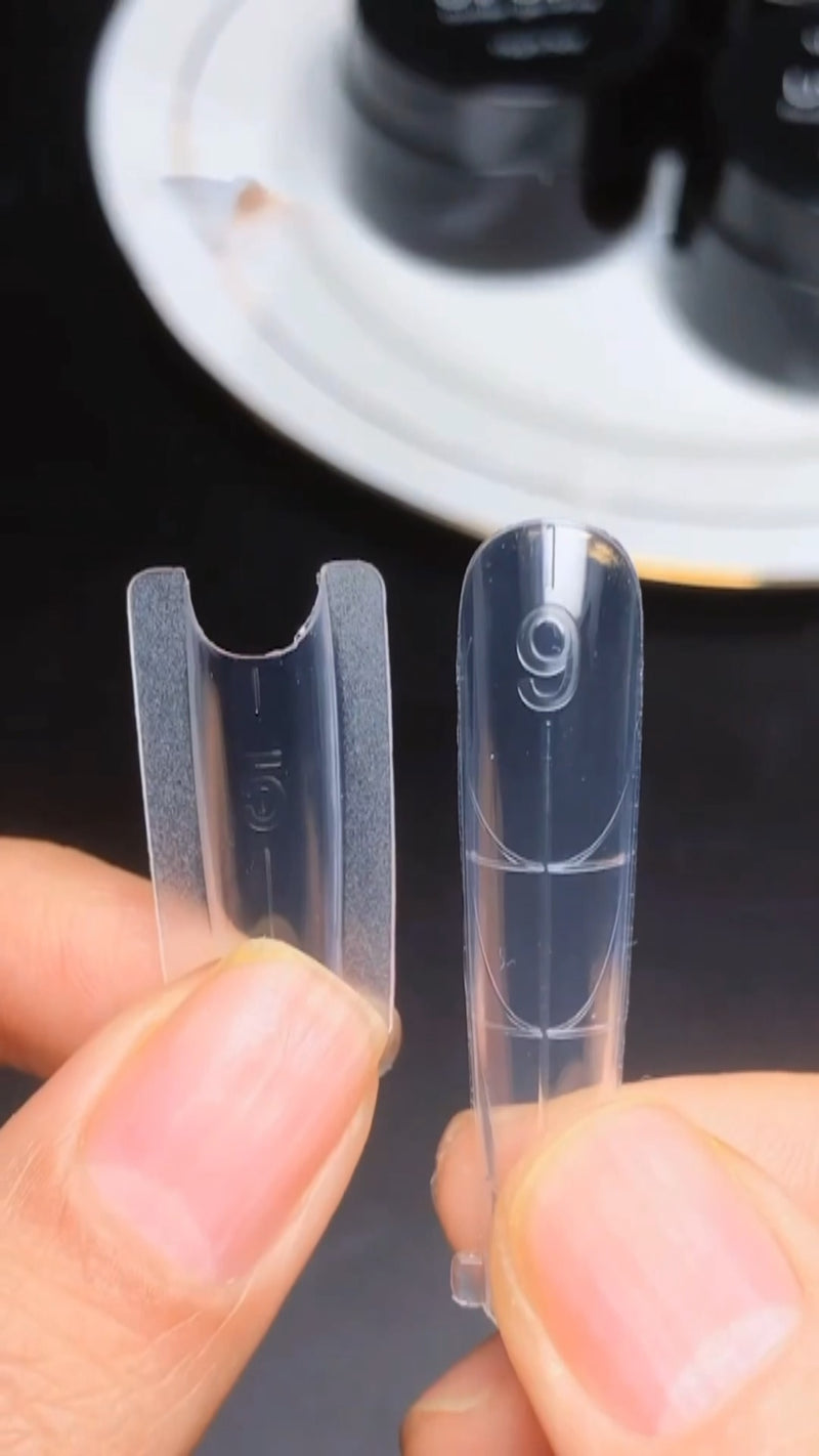 A clean close-up view of a clear plastic dual form being snapped off a newly cured clear polygel extension, leaving behind a glass-smooth surface.