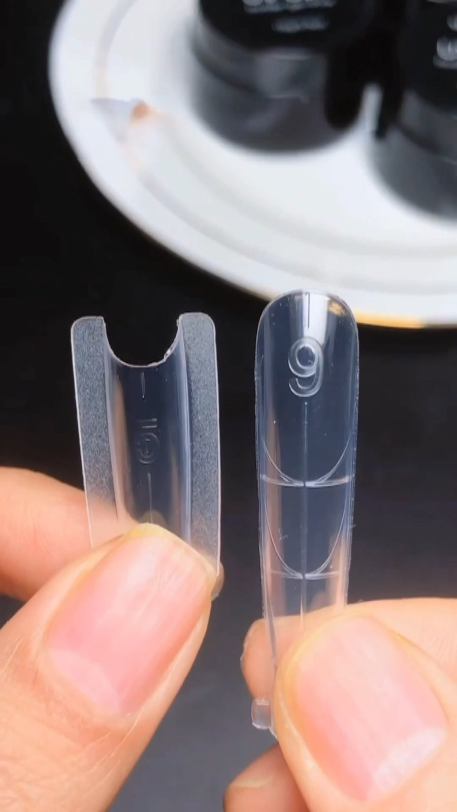 A clean close-up view of a clear plastic dual form being snapped off a newly cured clear polygel extension, leaving behind a glass-smooth surface.