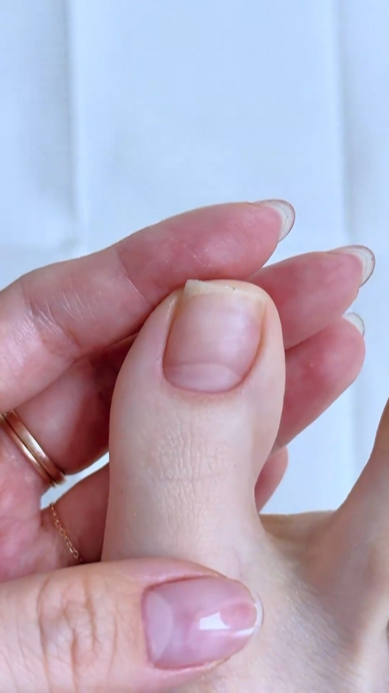 A clean close-up showing a hand gently pushing back cuticle tissue with a pusher tool as part of a casual home nail prep routine.